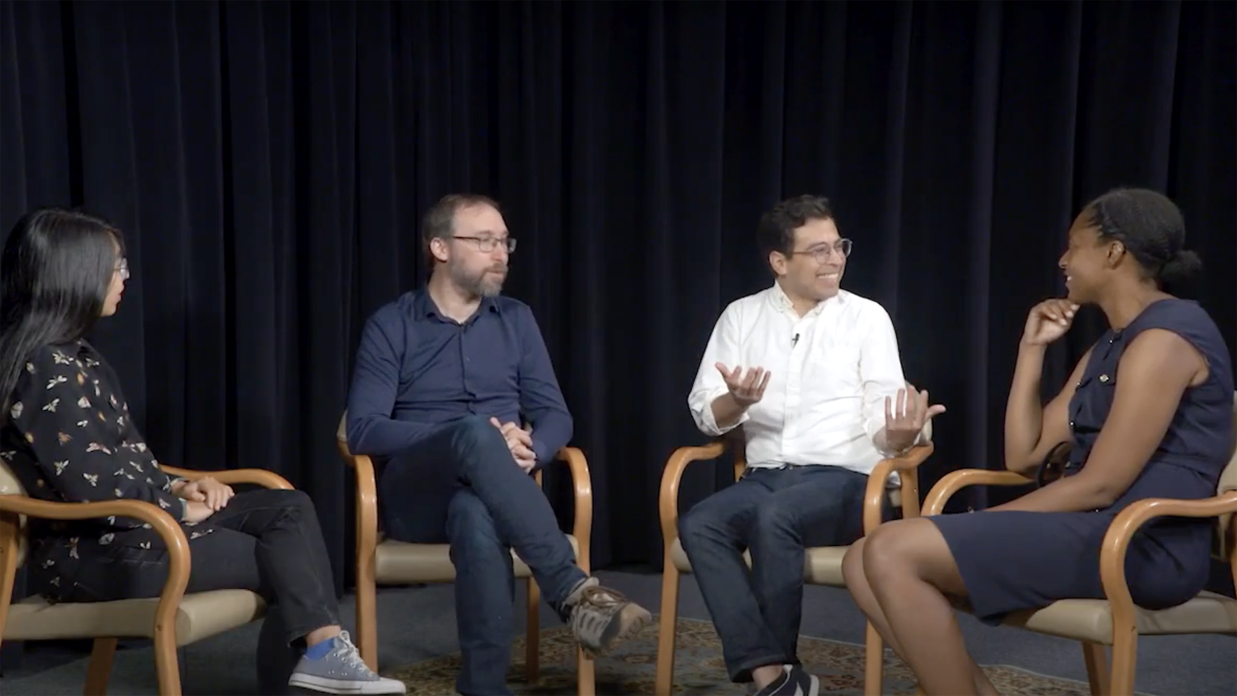 Aileen Liu, Hernan Garcia, Christian Paiz and Arianne Eason sit in chairs on a dark stage and talk