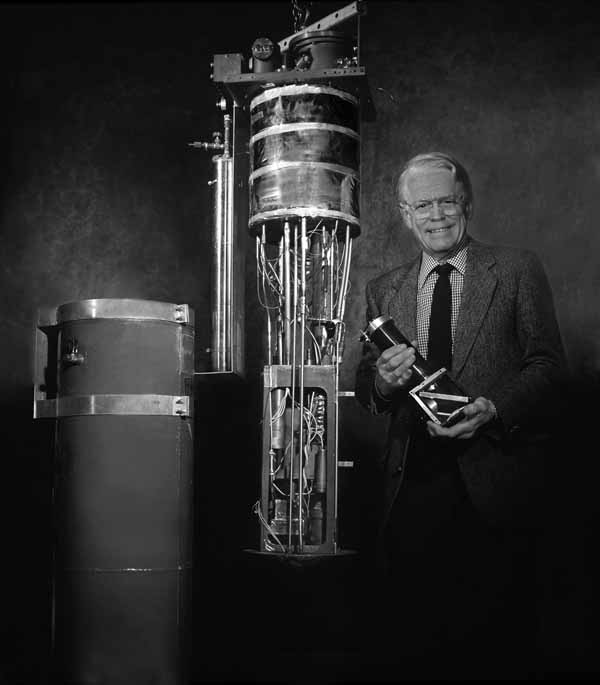 a smiling man standing next to an apparatus and holding a model of it