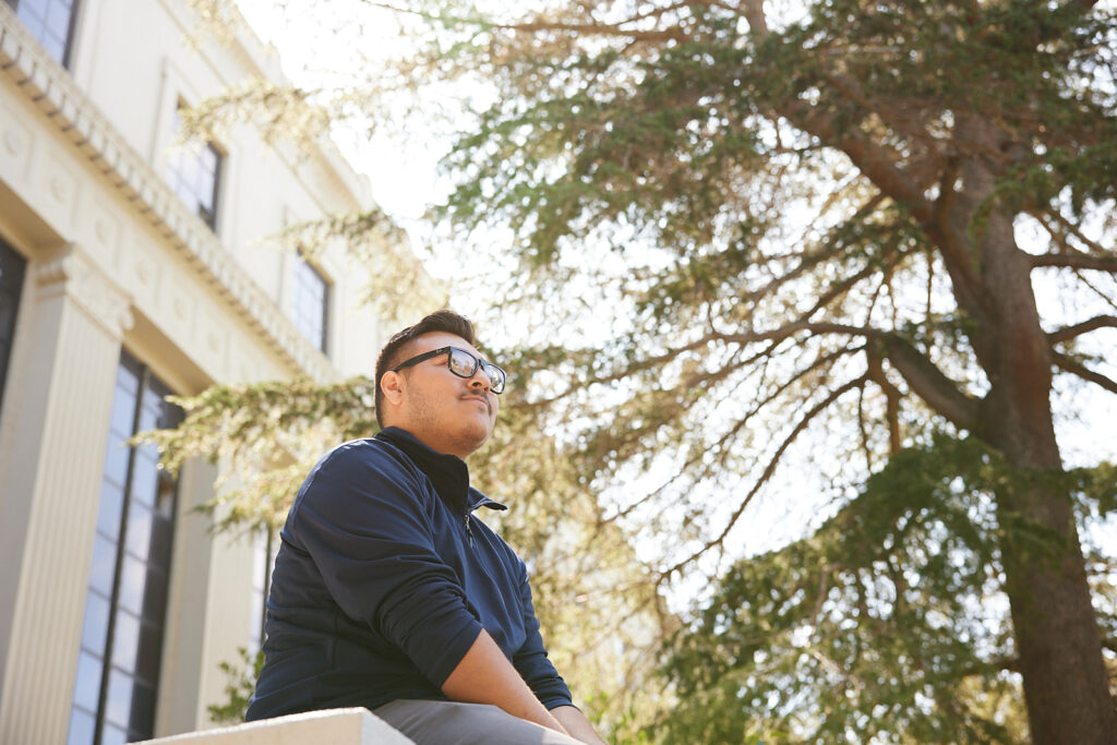 Student Soto Moreno, a political science major, sits outdoors on campus and looks up into the sky.