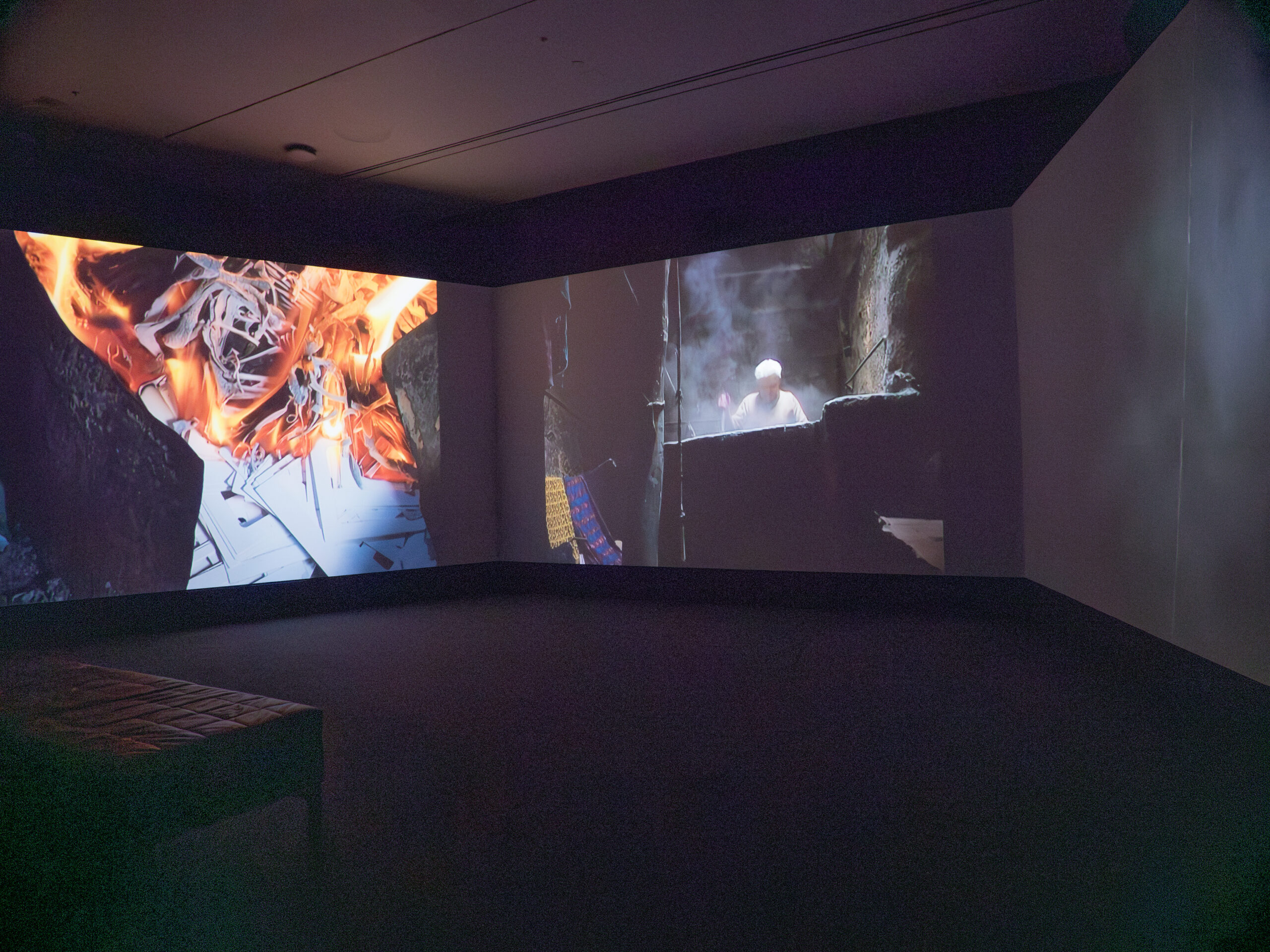 A photo showing three screens playing three videos, with one displaying a piece of paper on fire and another showing a man standing amid smoke