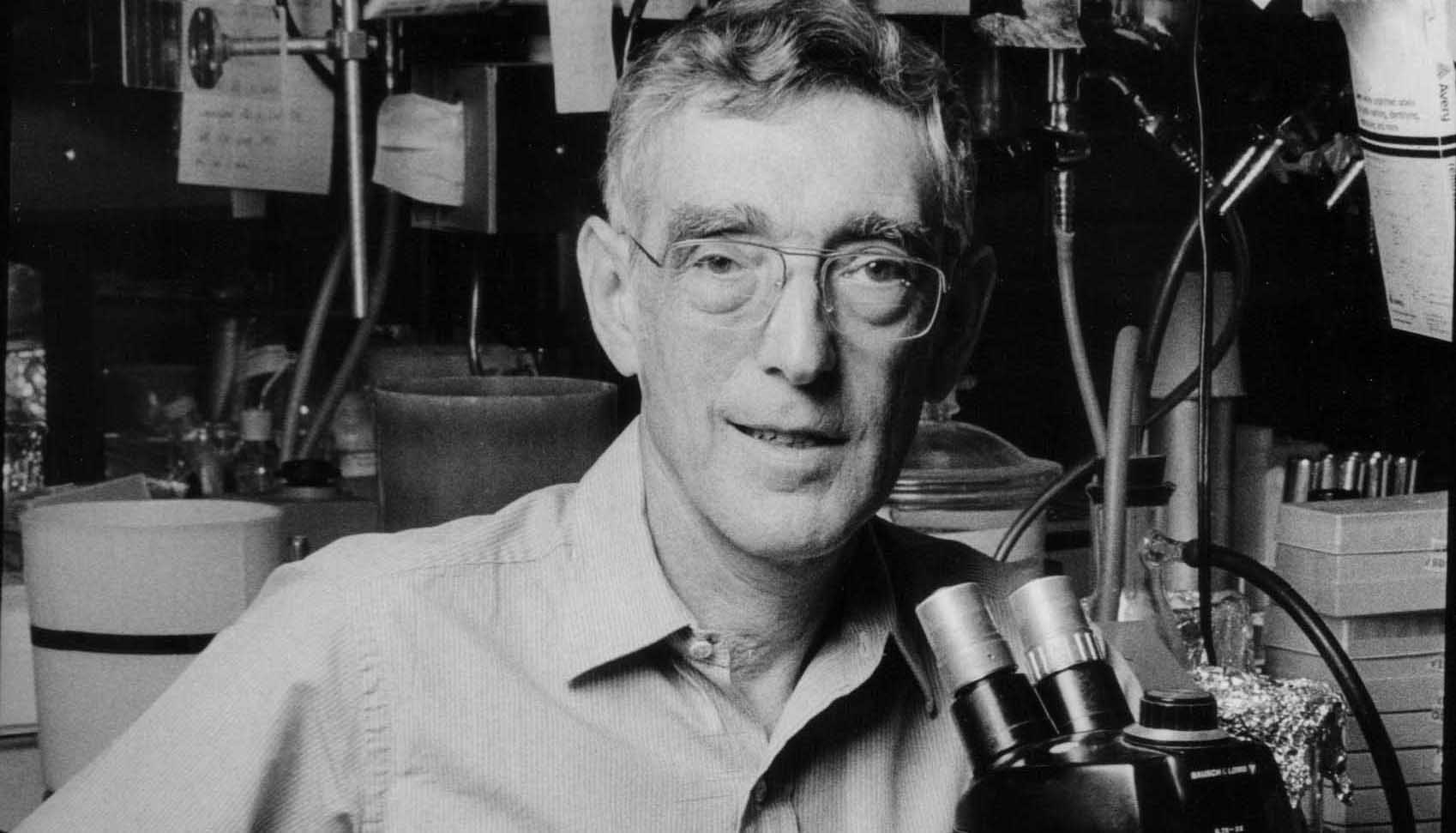 man in glasses next to microscope looking into the camera