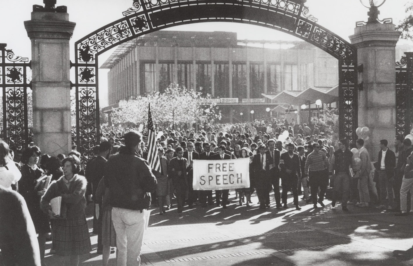 A historical photo of Mario Savio and other student protestors marching through Sather Gate on November 20, 1964