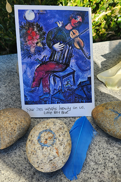 A gift for Nox, the falcon who died, below the Campanile includes several painted rocks, a blue feather and a small reprint of a painting with the words "Your loss weighs heavily on us Little Boy Blue."