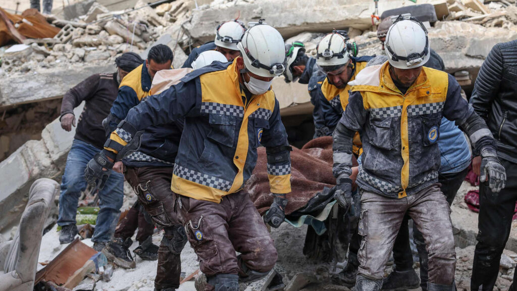 About a dozen volunteer rescue workers wearing GoPro cameras on their white helmets, carry a person on a stretcher out of rubble in Syria