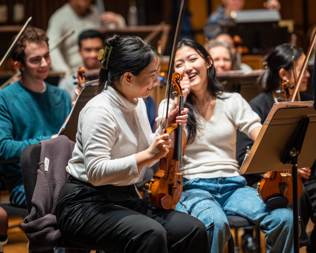 Students in an orchestra at UC Berkeley smile and hold their instruments.