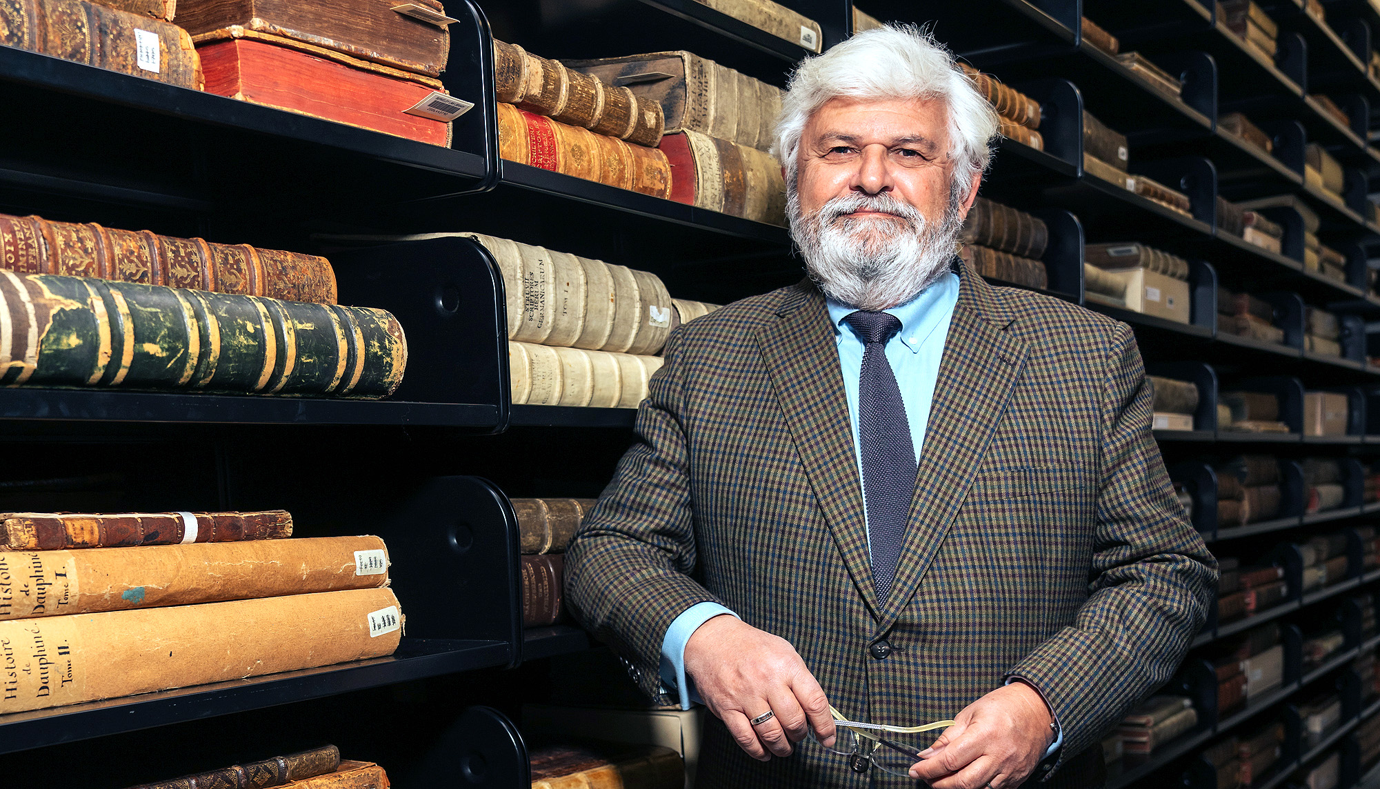 Law Professor Laurent Mayali standing causally before racks of antique bound legal documents