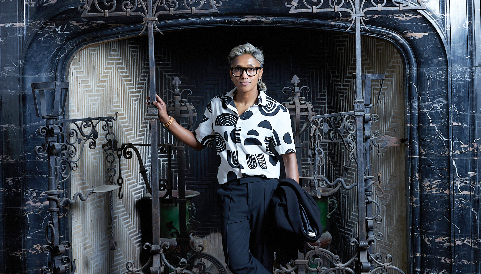 Poulomi Saha stands in front of a huge fireplace surrounded with decorative wrought iron.