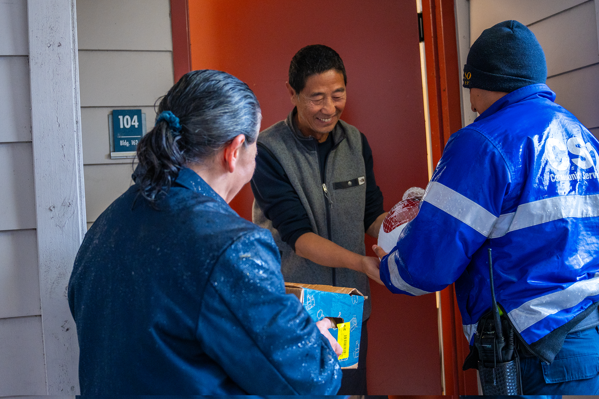 A smiling man standing in a doorway received a box handed to him by two people