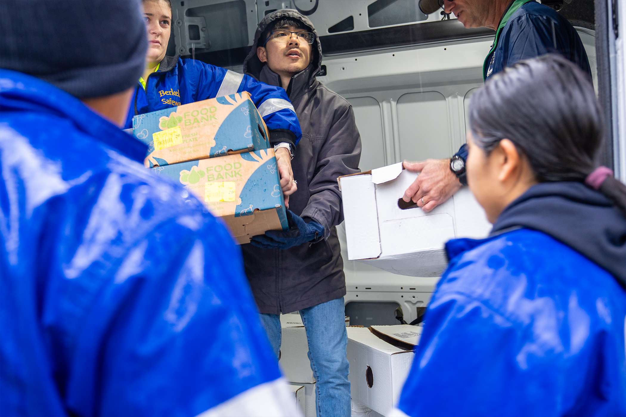 People inside a vehicle hand boxes of food to others outside the vehicle while also coordinating where the various apartments are located.