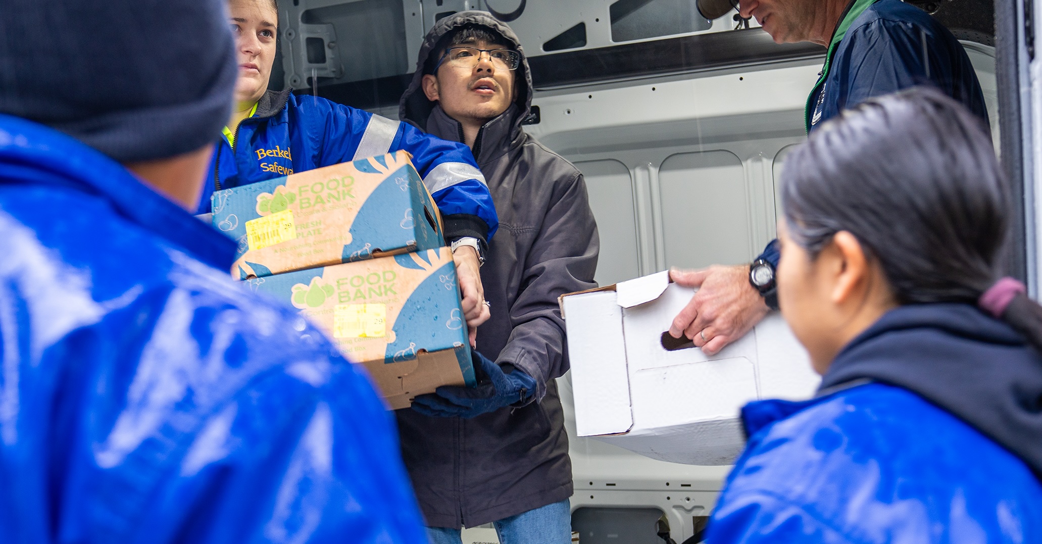 People inside a vehicle hand boxes of food to others outside the vehicle while also coordinating where the various apartments are located.