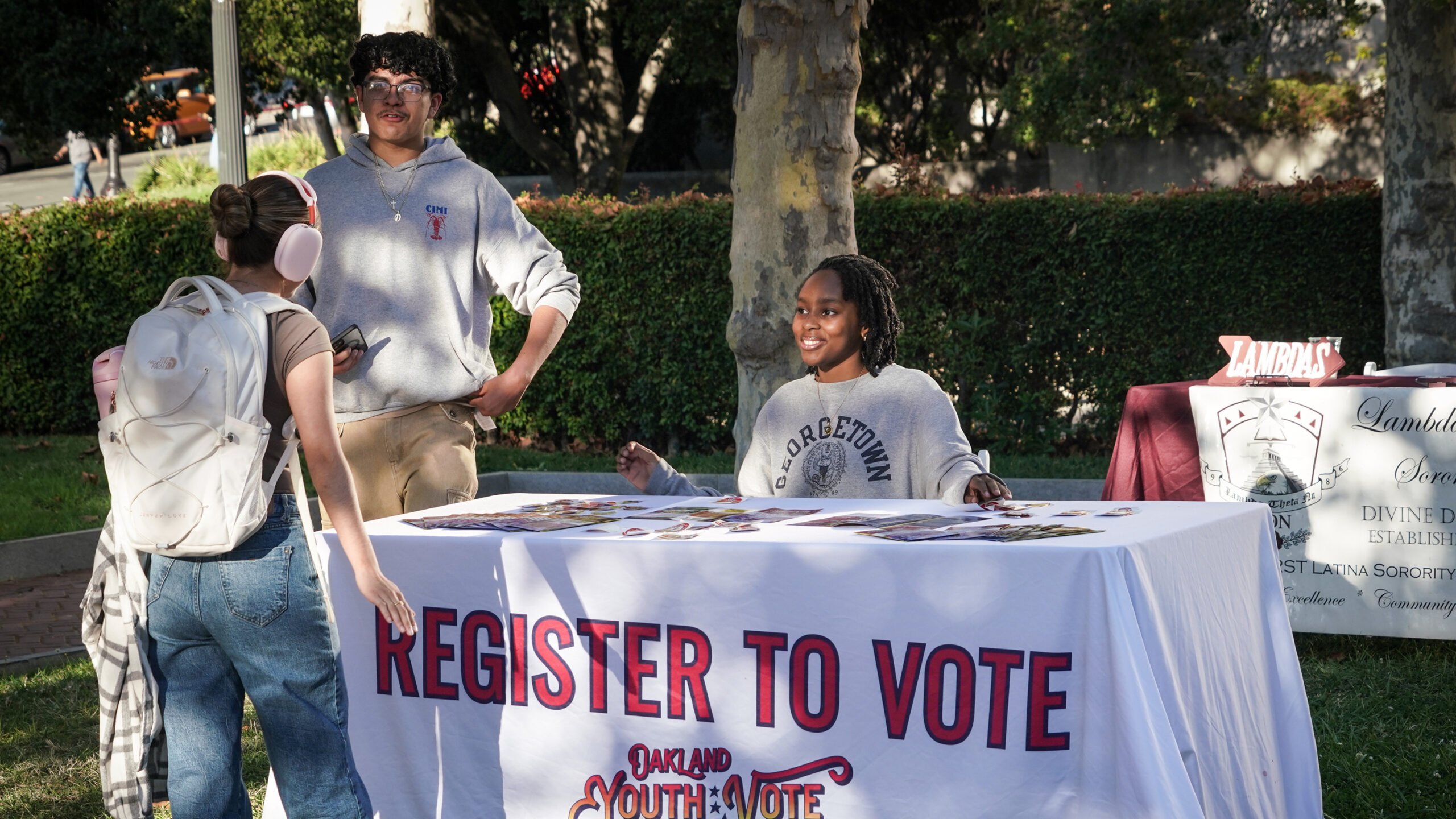 a student sits at a voter registration table and smiles as another student approaches