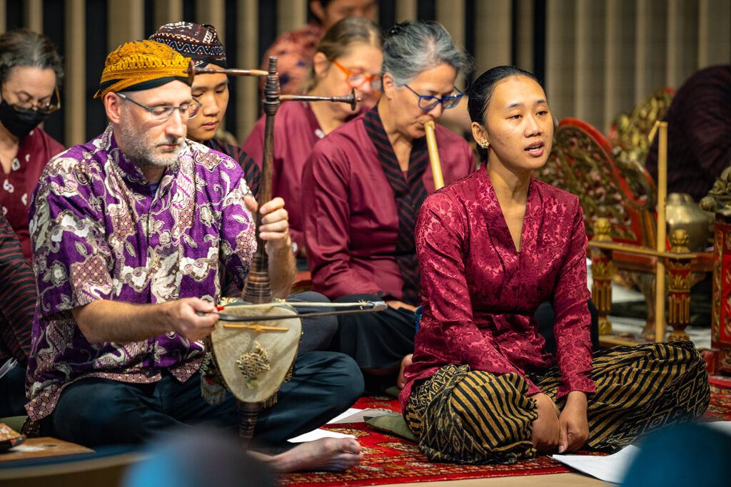 An ensemble plays the campus's Indonesian (Balinese) gamelan on the Wu Hall stage. They are mostly sitting on the floor with various instruments.