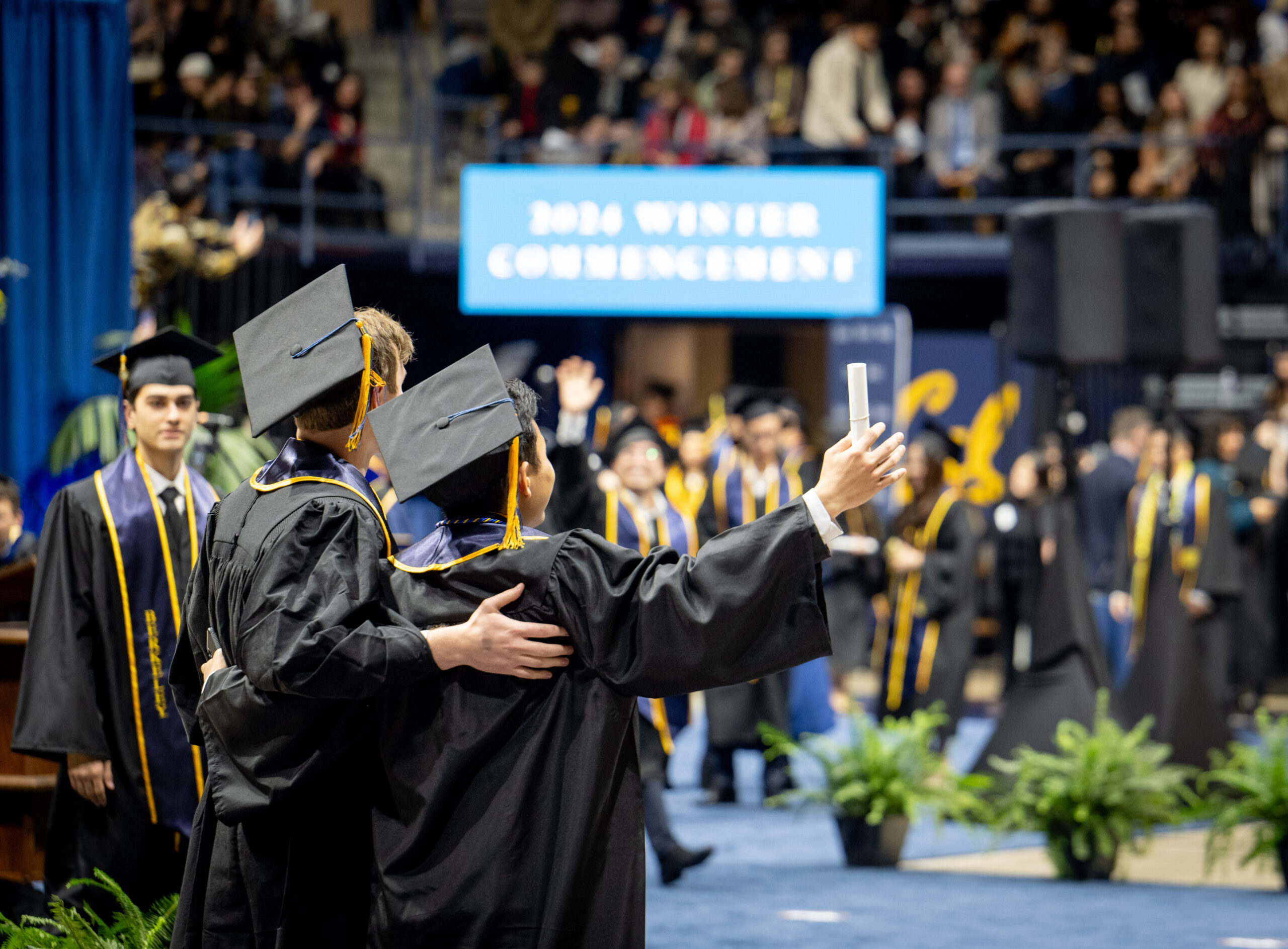 Two new UC Berkeley graduates embrace before the crowd at Winter Commencement 2024.