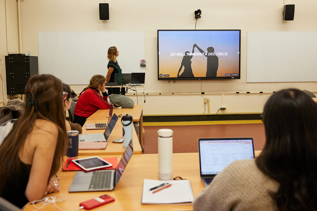 Student in an upper division Italian class look at a screen at the front of the room where a scene is playing from My Brilliiant Friend, an HBO series based on the novels by Elena Ferrante.