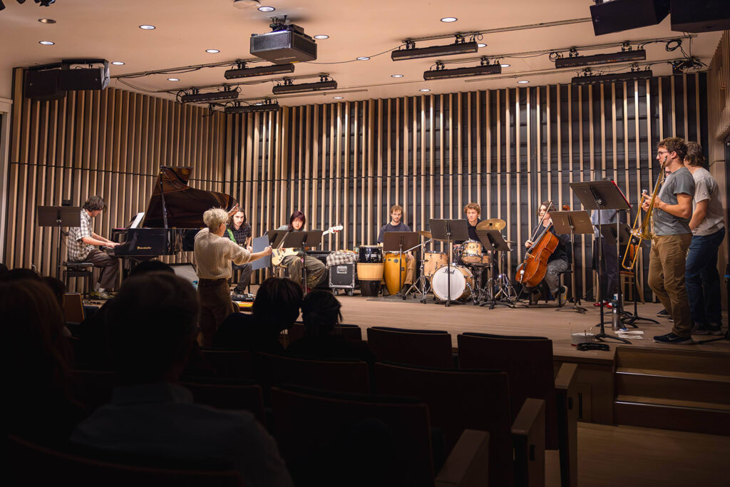 At a new concert venue in Wu Hall, in Morrison Hall, the UC Nu Jazz Collective plays on stage, with the dark silhouettes of audience members in the foreground.