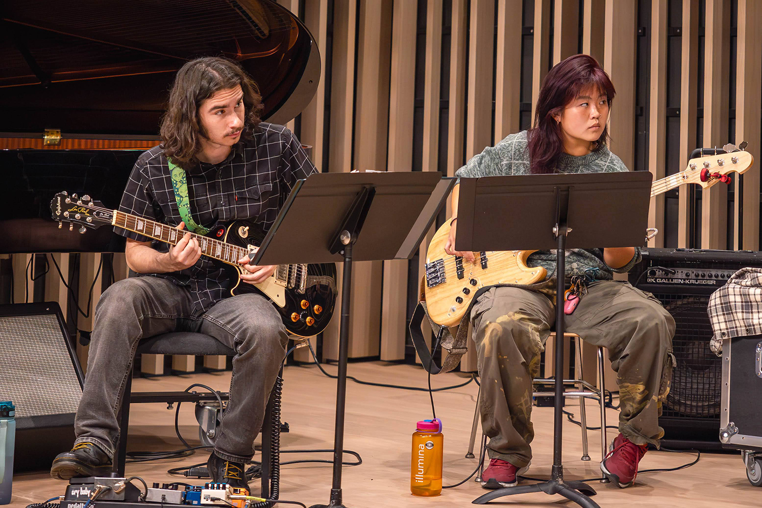 Two musicians in the UC Nu Jazz Collective play guitar onstage in the emsemble at a performance at Wu Hall, a new venue in Morrison Hall. The students are seated with music stands in front of them and their amplified guitars in their grasp.