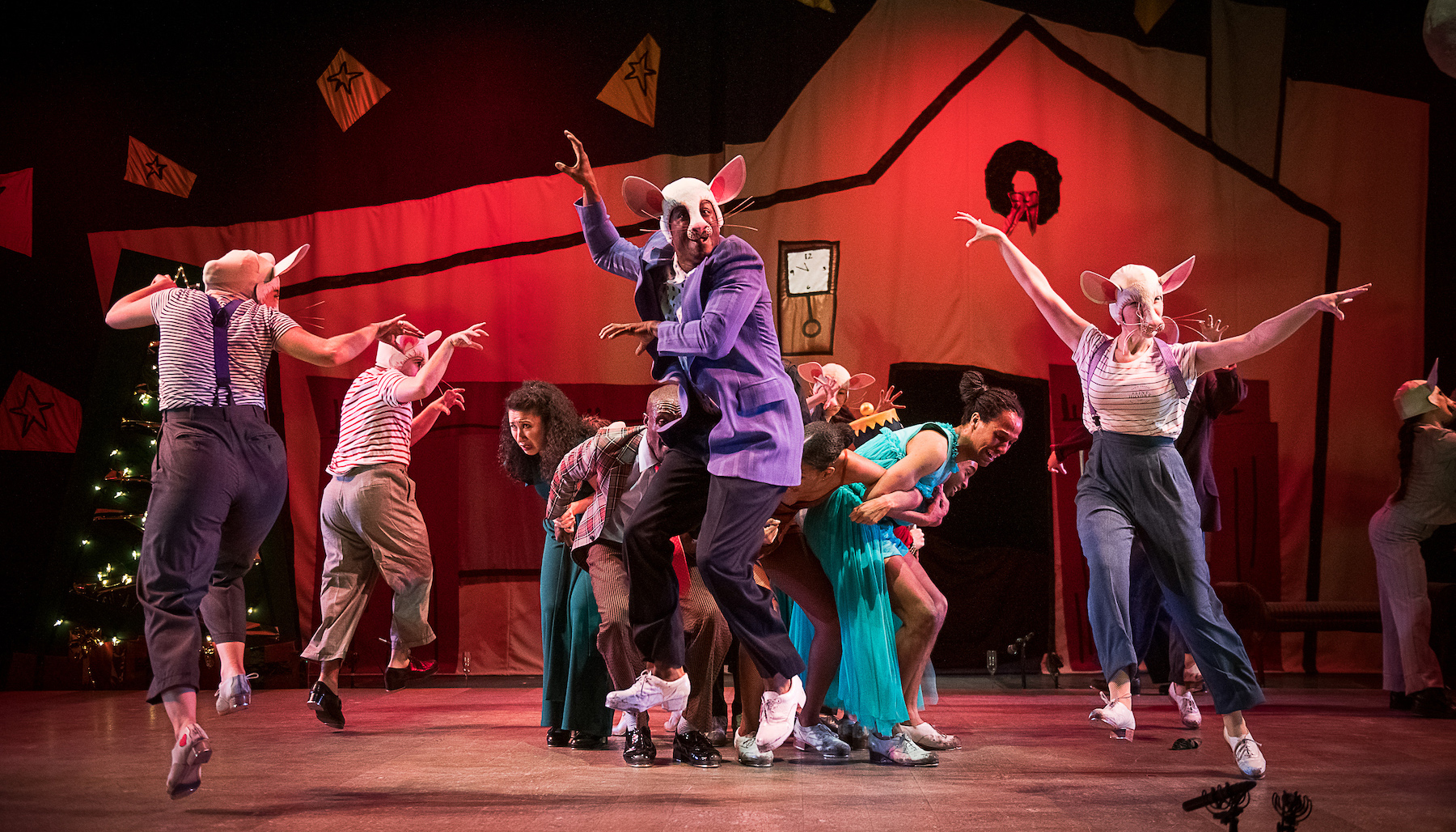 about a dozen dancers in the nutcracker suite perform on stage. six are wearing rat masks and dancing around a group of dancers who look frightened.