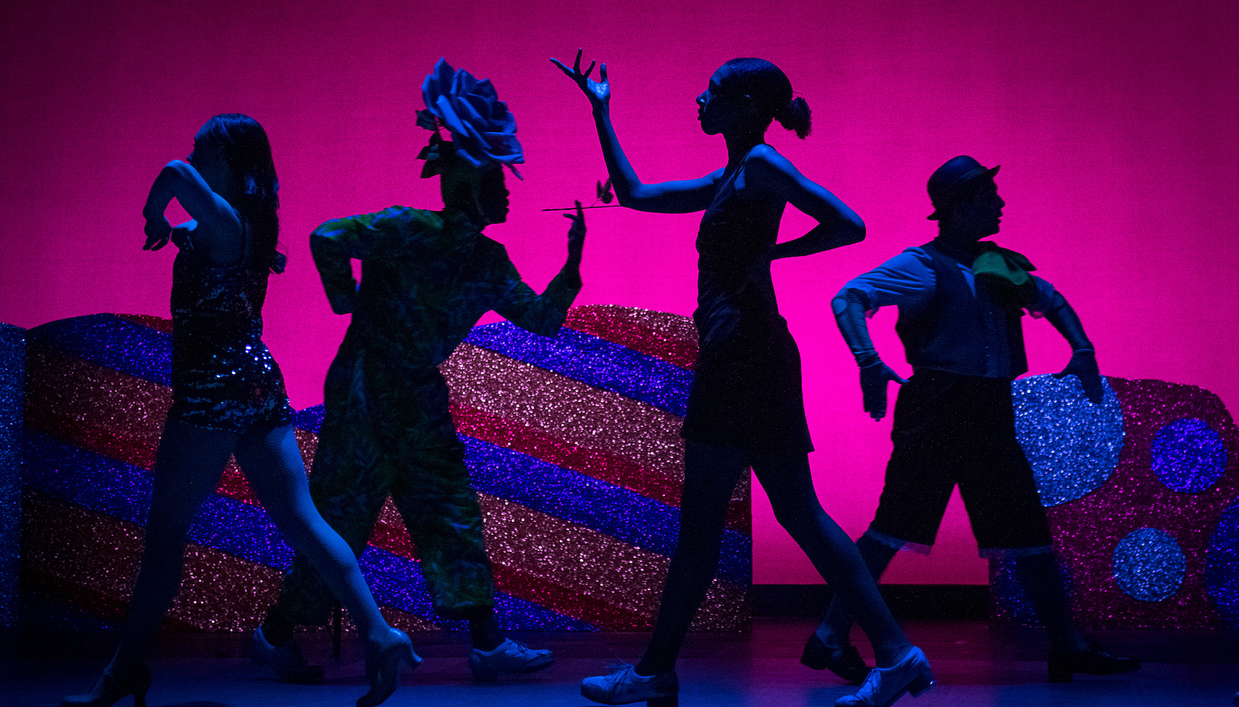 silhouettes of four dancers in the nutcracker suite pose on stage with a pink and sparkly background