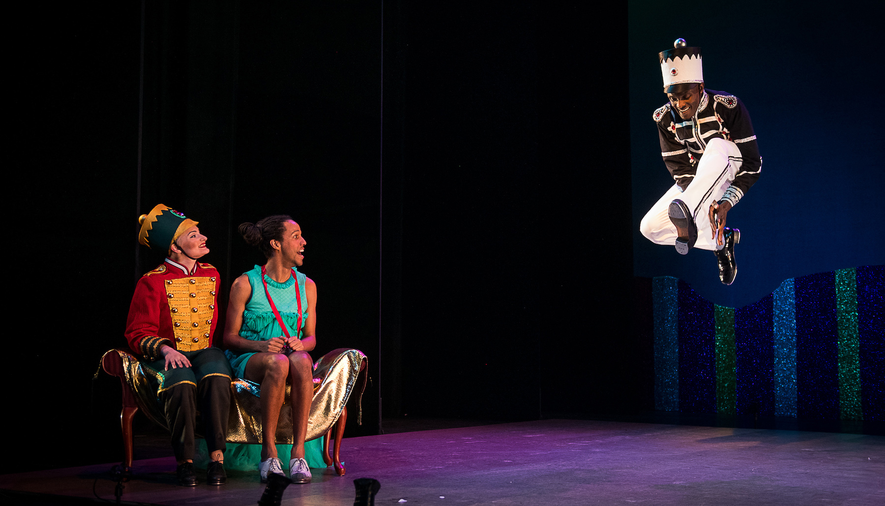 three dancers in the nutcracker suite - one dancer is jumping high in the air, while two others are sitting on a bench watching