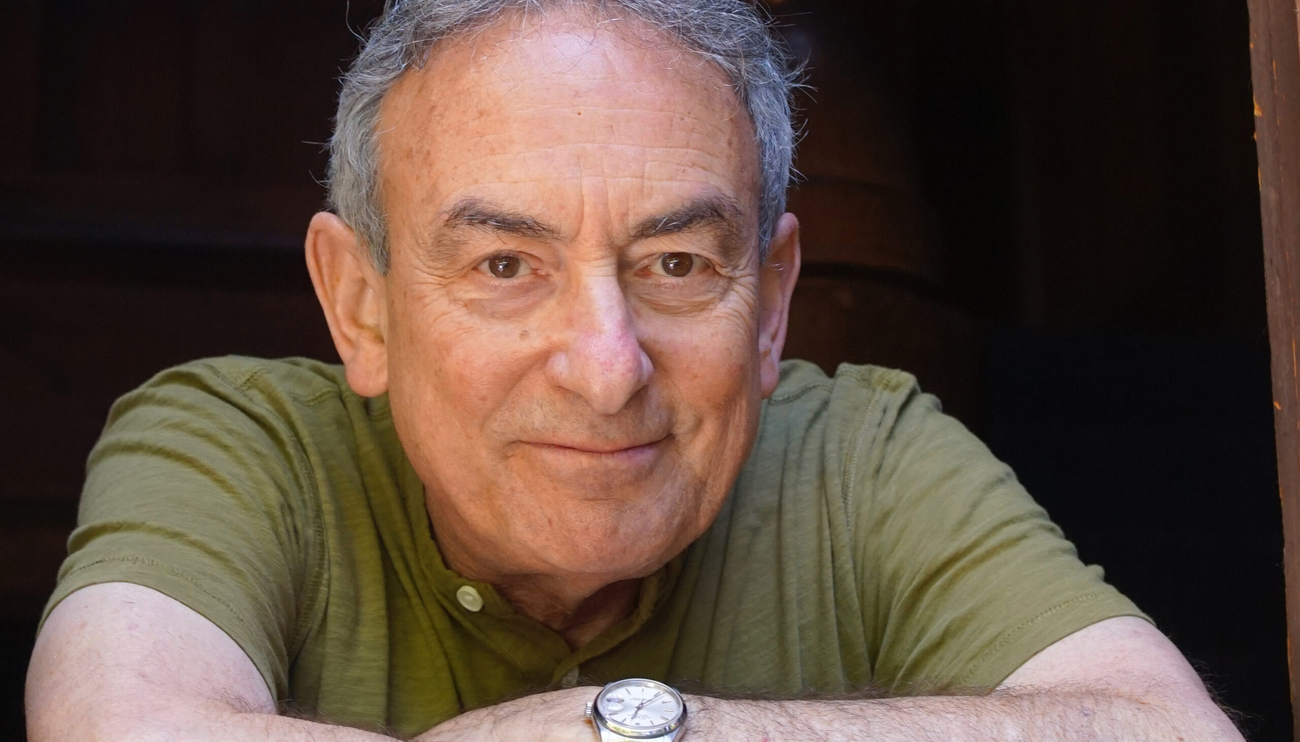 smiling man with gray hair staring at camera with arms crossed