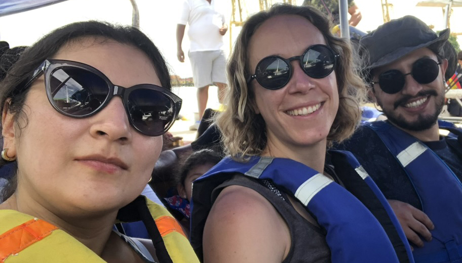 two women and a bearded man, all wearing sunglasses, smiling for a selfie aboard a boat