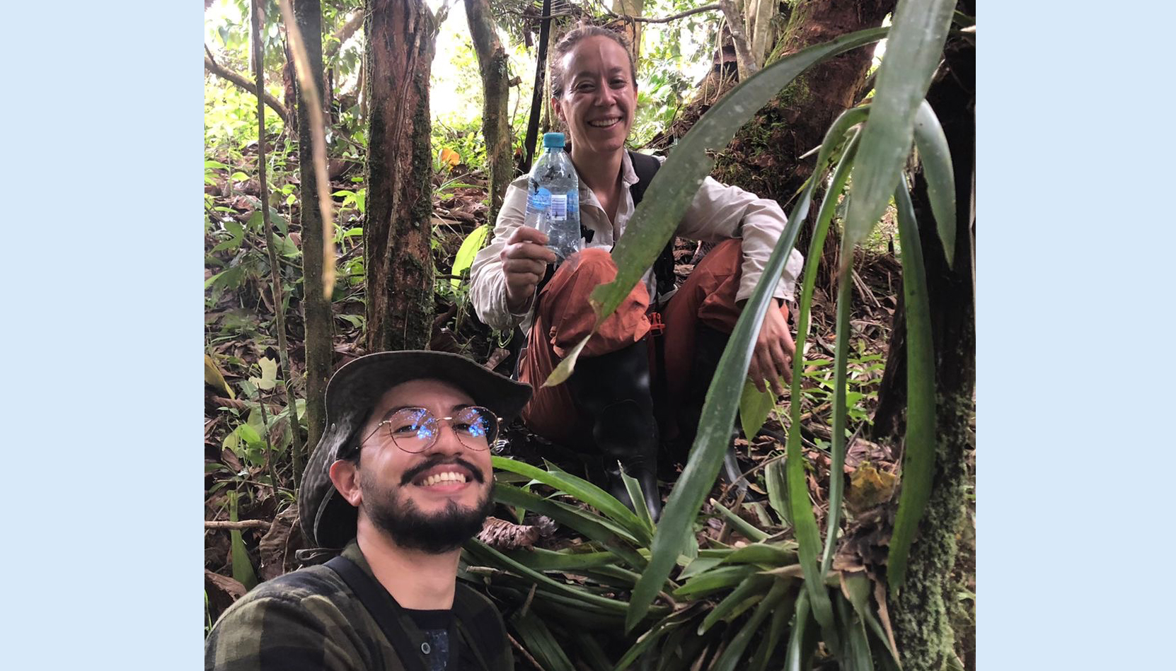 a smiling woman holding plastic water bottle, perched above a bearded man in hat and glasses