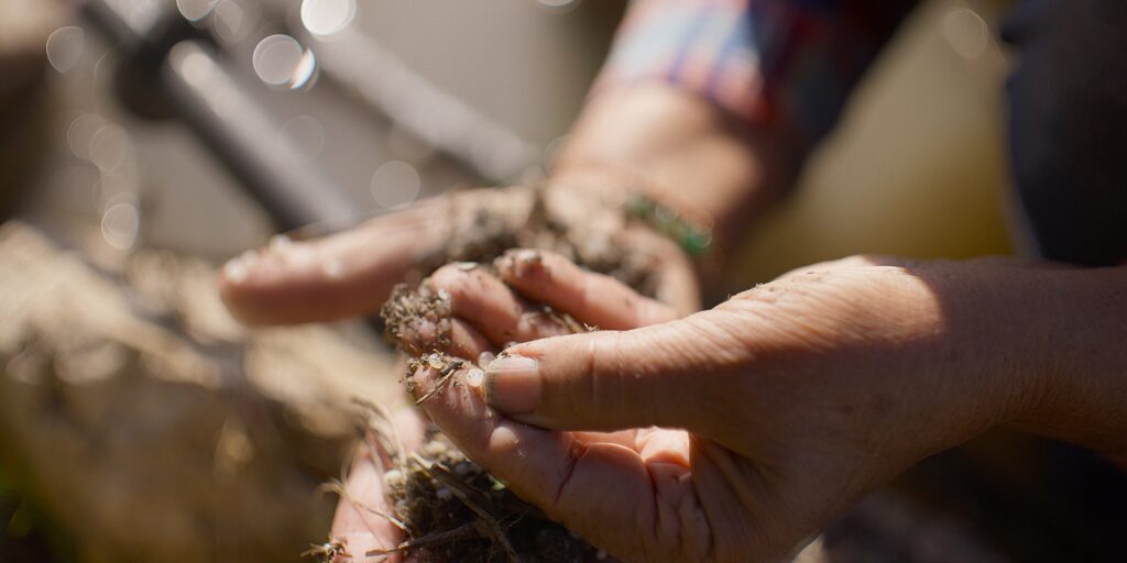 A still from "Plastic People," showing someone handling dirt laced with plastic pieces.