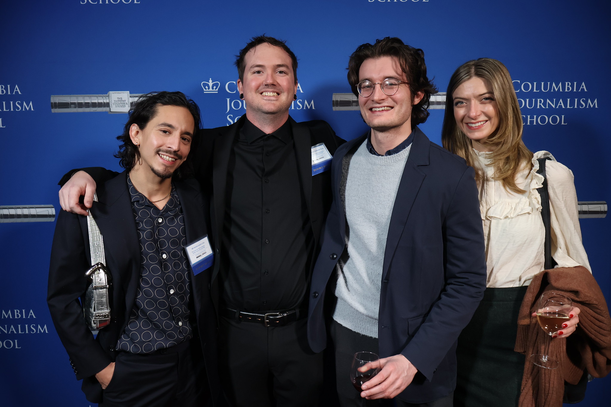 four people, the left two wearing name tags, stand in front of a blue backdrop that says Columbia University. They are smiling broadly.