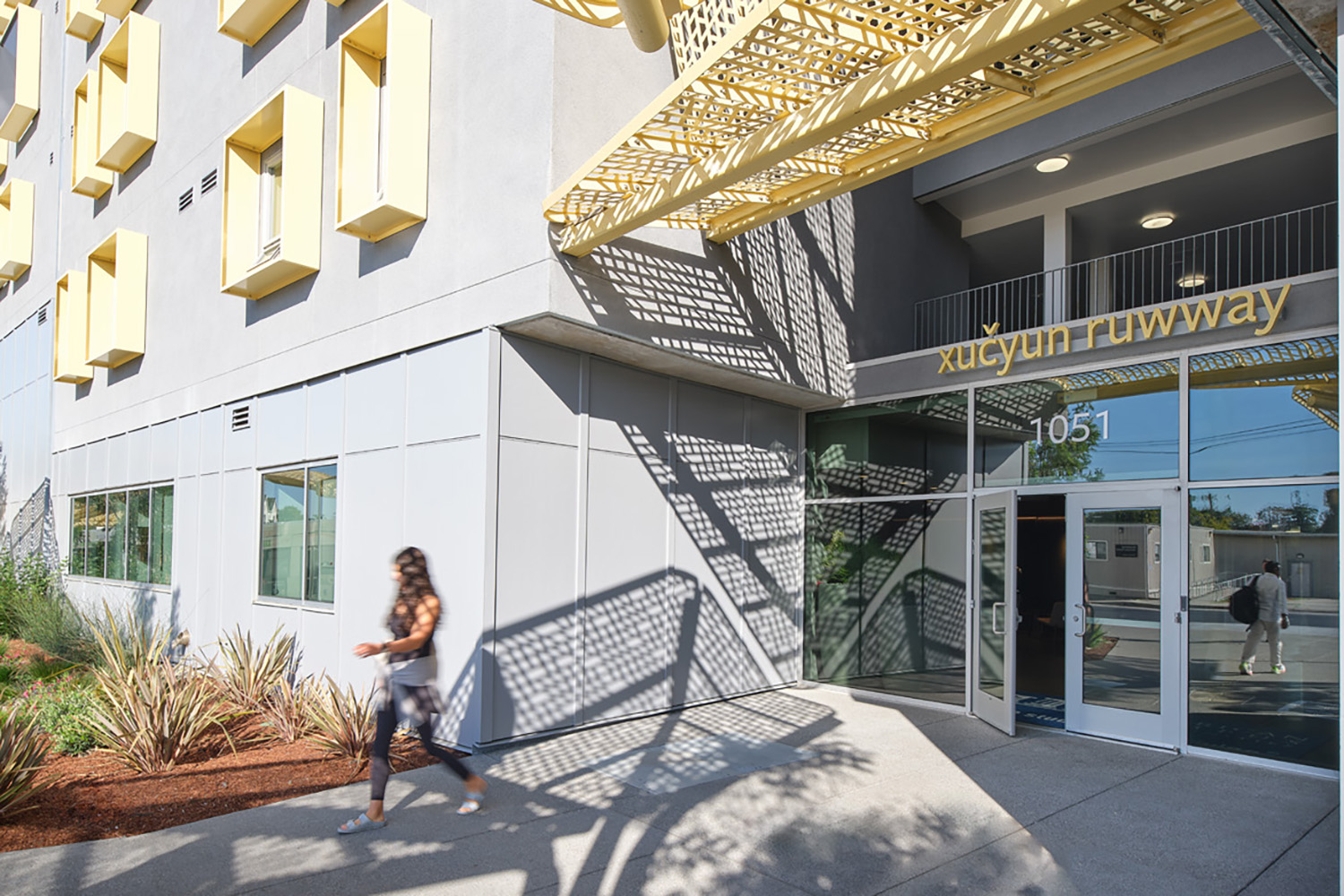 A main entrance to xučyun ruwway graduate student housing has the Chochenyo name spelled just above the front door. The metal lettering is painted yellow.