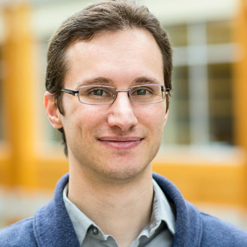 headshot of a man in glasses wearing a collared shirt and weater