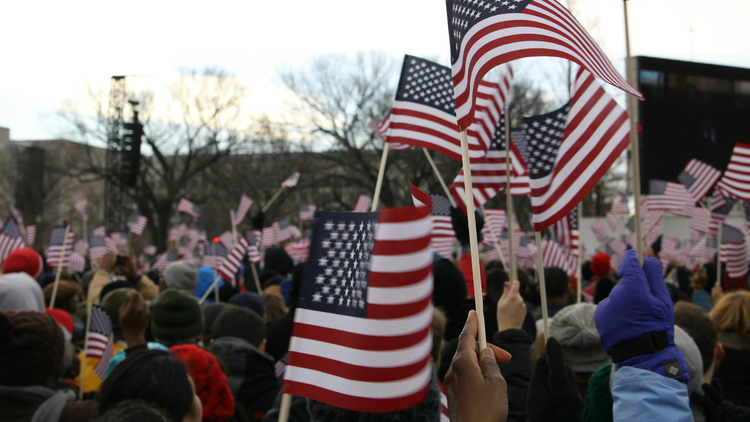 a large crowd of people wave small American flags at a political gathering outside