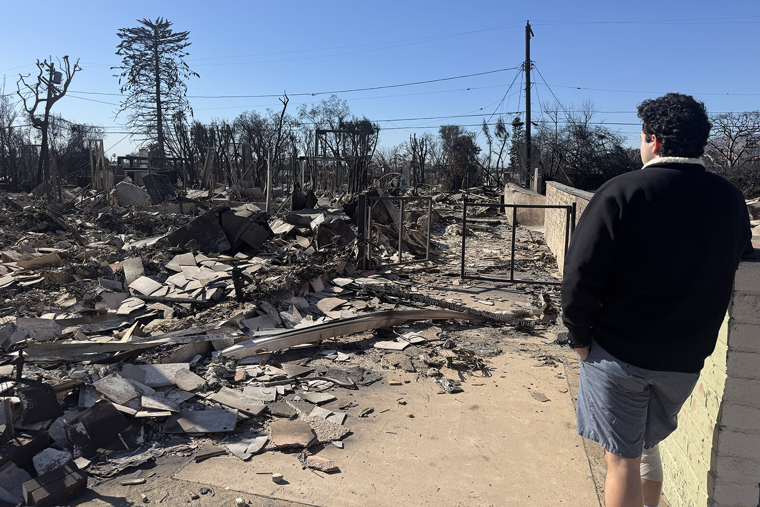 After the Palisades Fire, student Max Rodman looks at the rubble that once was his family home. His knee is wrapped because he was recovering from surgery.