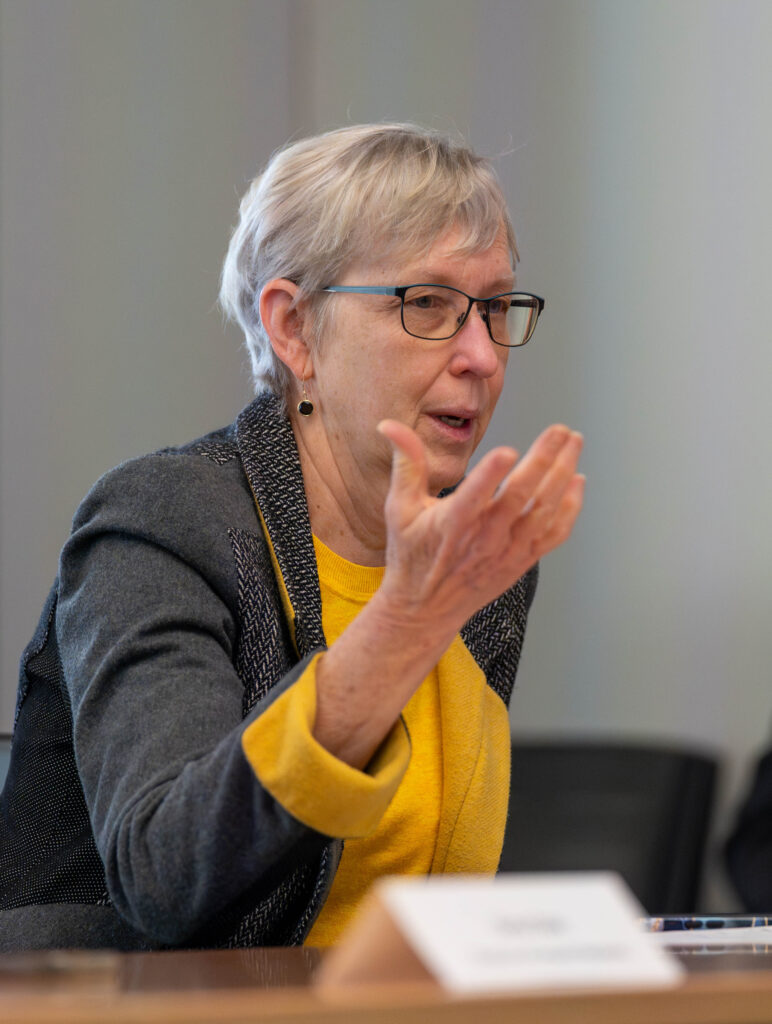 a woman with glasses and a yellow blouse gesturing while talking