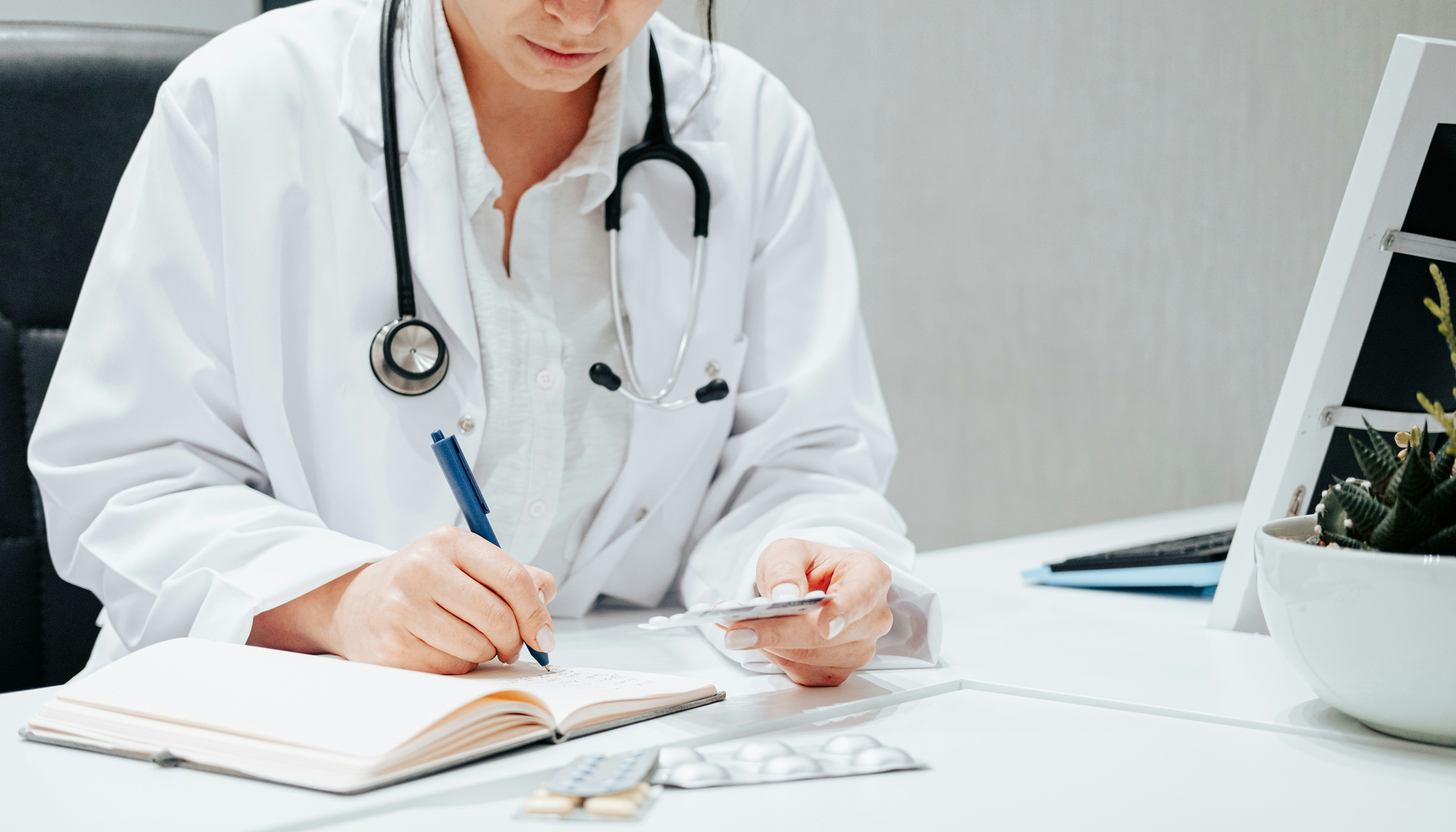 a doctor writes in a notebook while she examines medicine held in the other hand