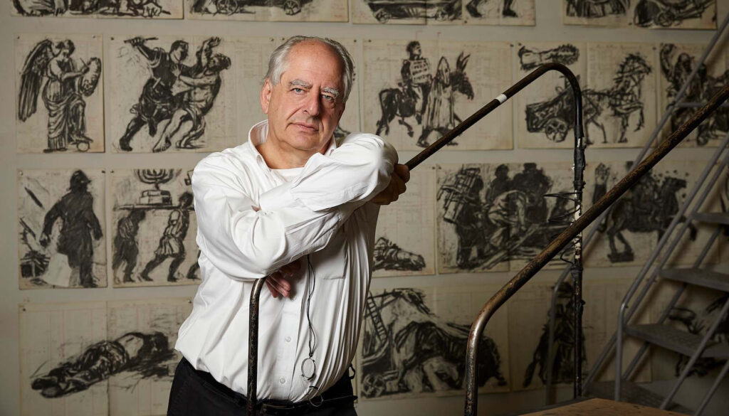 William Kentridge poses in front of a wall of his charcoal drawings