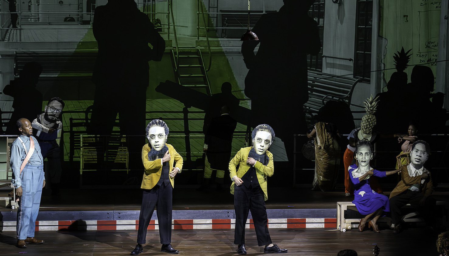 A performance on stage of the chamber opera The Great Yes, The Great No. A handful of performers dance wearing large photographs of famous artists and thinkers as masks.