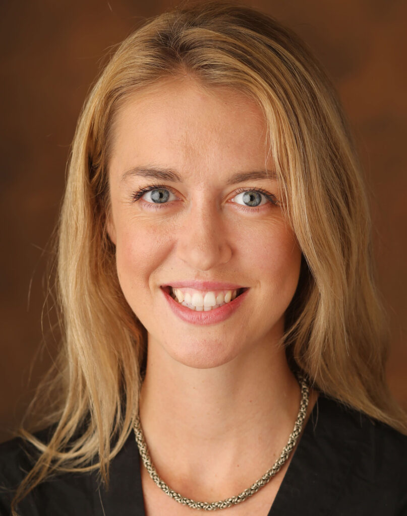 headshot of Amanda Clayton, smiling, against a brown backdrop