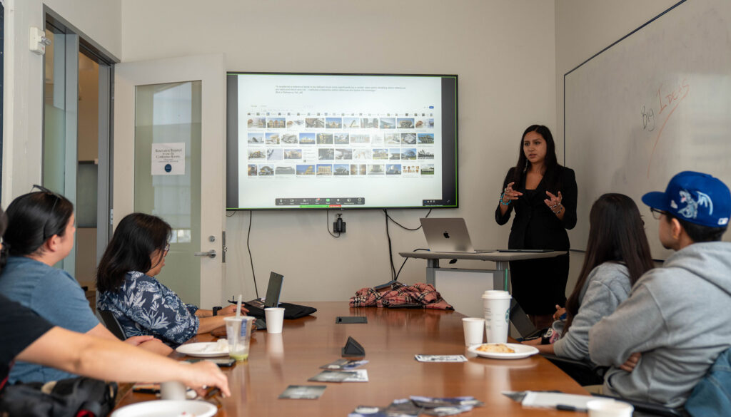 Students sit at a conference table watching a person give a presentation.