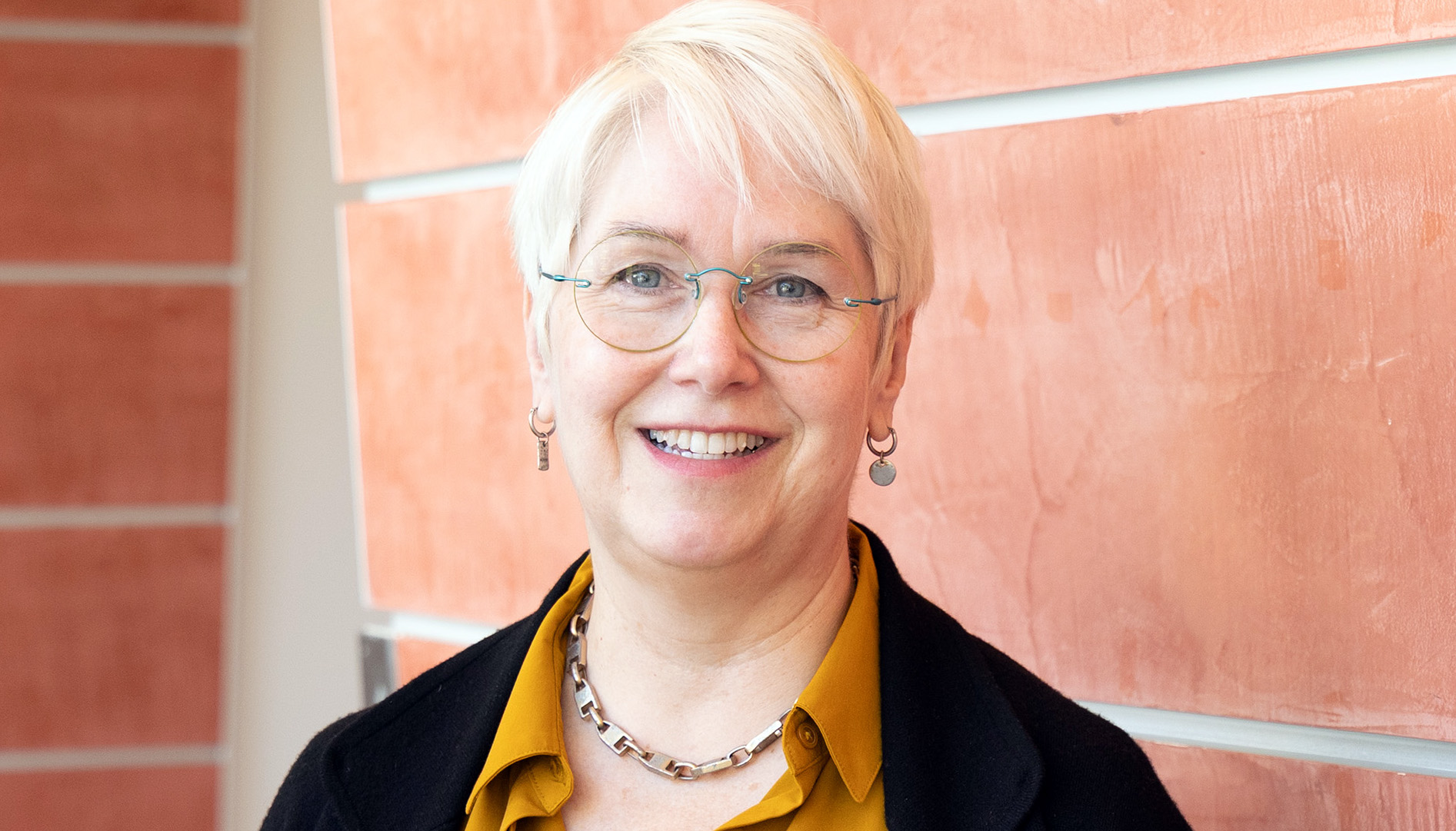 smiling woman with white hair and glasses wearing a mustard blouse with black jacket