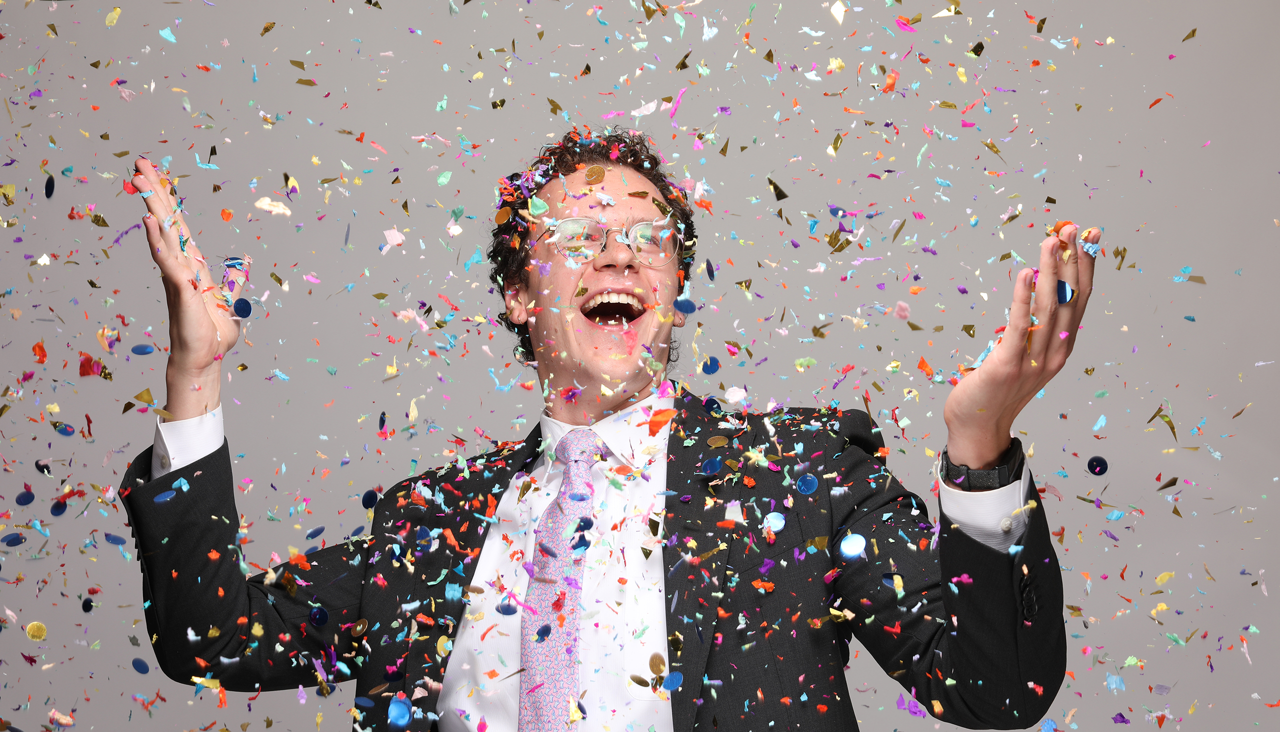 Frank Cahill smiles and holds up his hands as colorful confetti is all around him, showing the fun, playful spirit of the spelling bee and the people who run it
