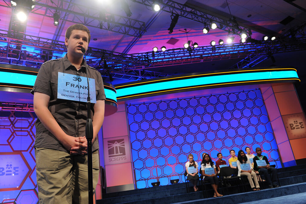 Frank Cahill at age 14 spells a word at a microphone during the spelling bee in 2012 while the other contestants look on from their seats