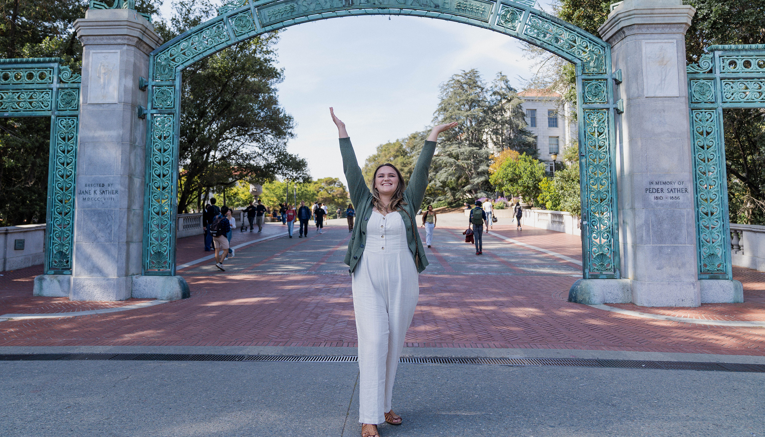 Emily stands under Sather Gate, smiling with her arms stretched in the sky