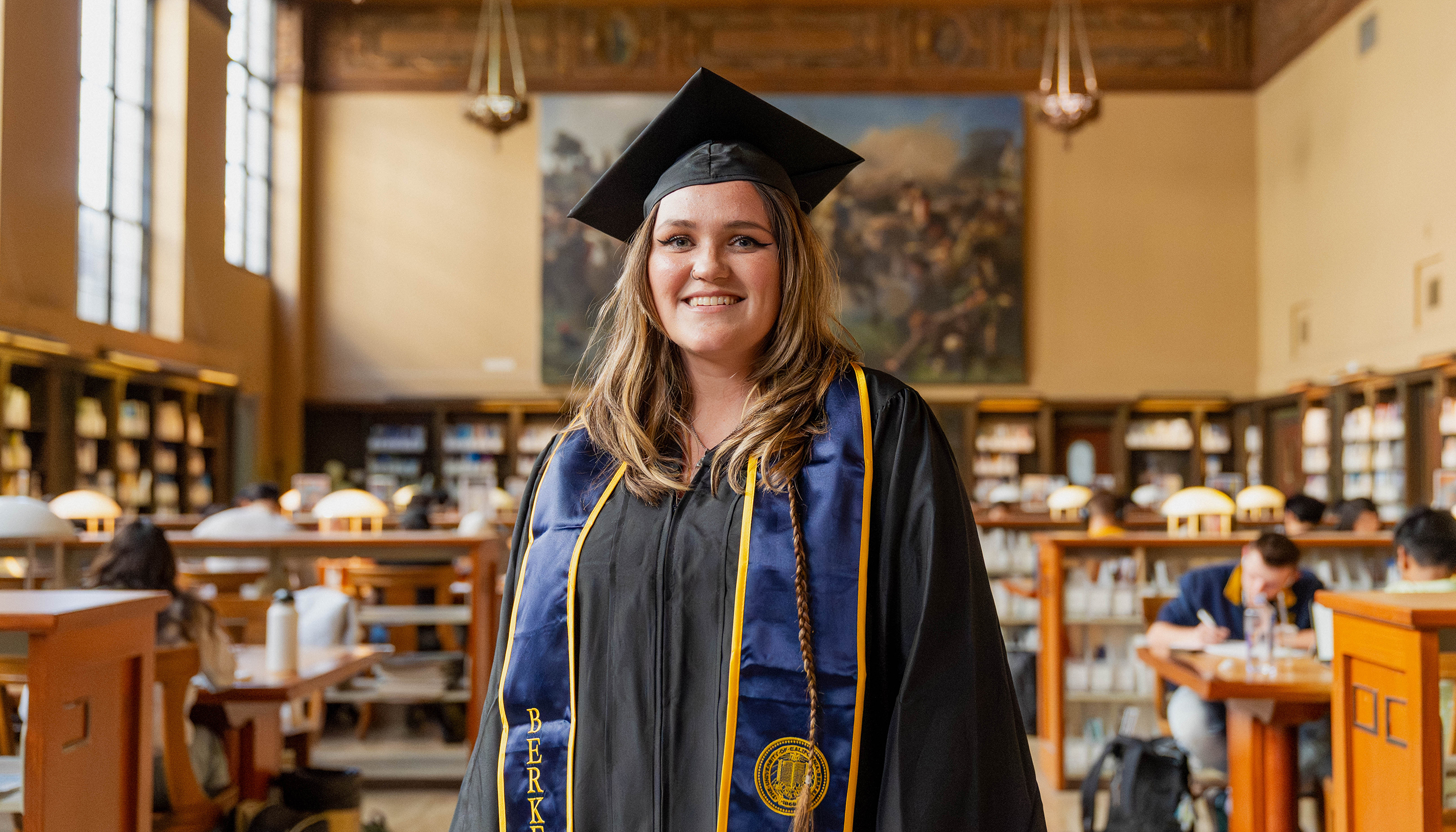 Portrait of Emily Thompson in her cap and gown in the UC Berkeley Library