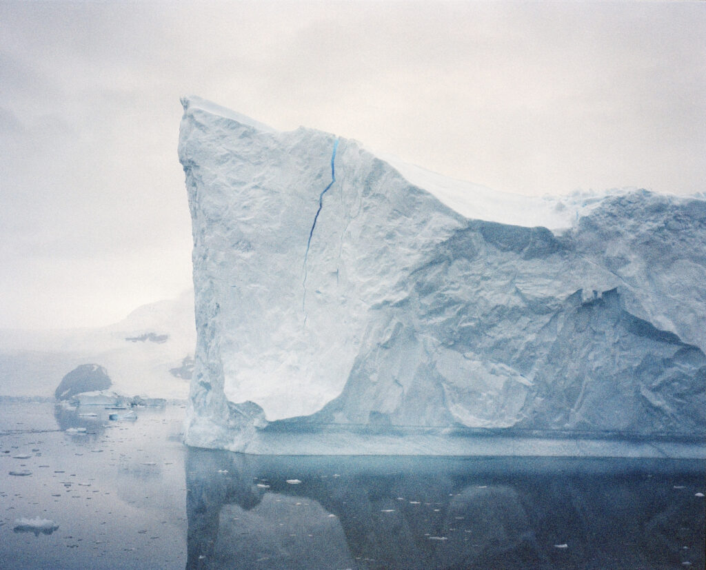 a striking image of an iceberg, with very textured, craggy sides, rising out of pale blue water
