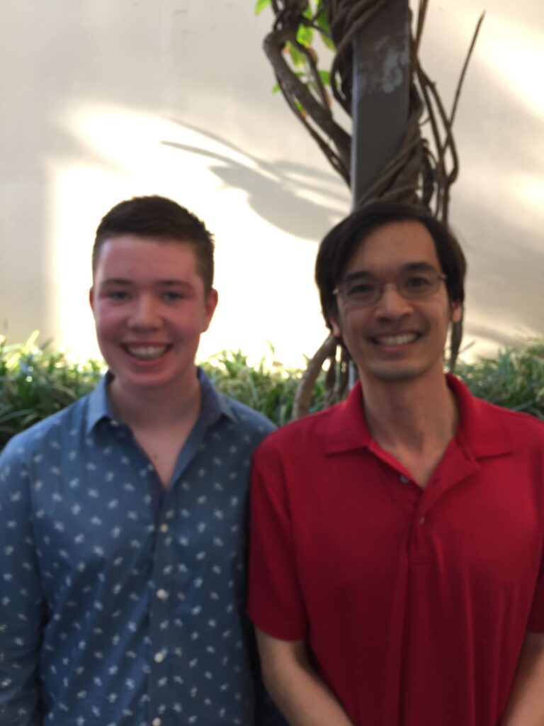 a boy in a collared shirt smiles next to a man in glasses and a red polo.