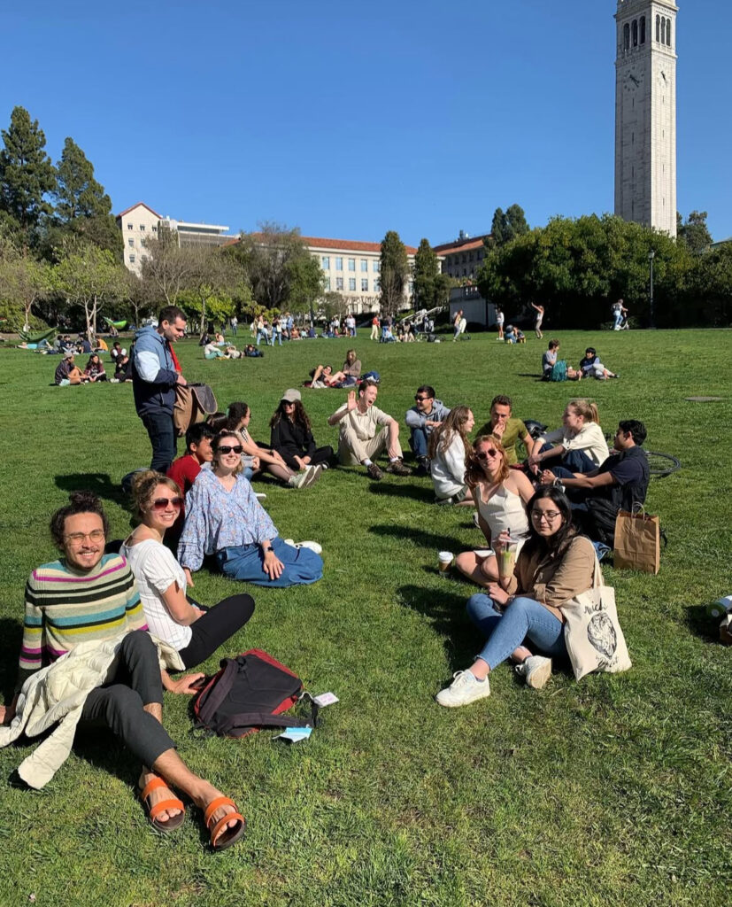A group of students, many wearing sunglasses, sit in Memorial Glade.