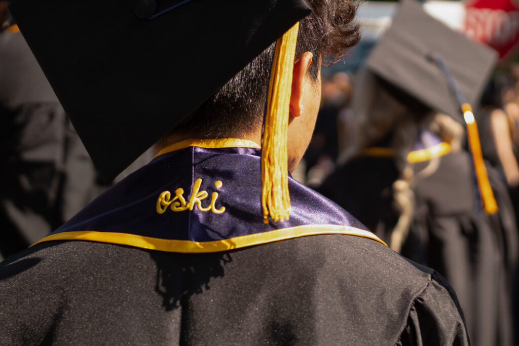 the back of a graduate's head, with the gold tassel visible. His blue sole is embroidered with the cursive word "oski"