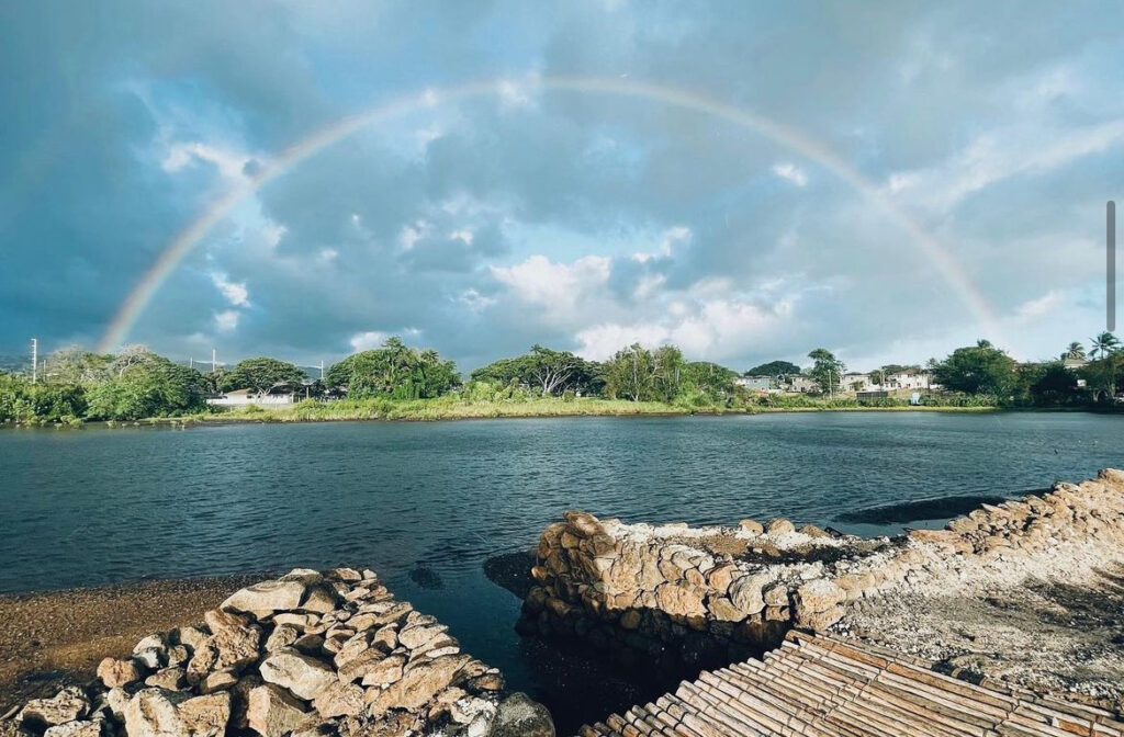 A rainbow appears over a large clear pond.