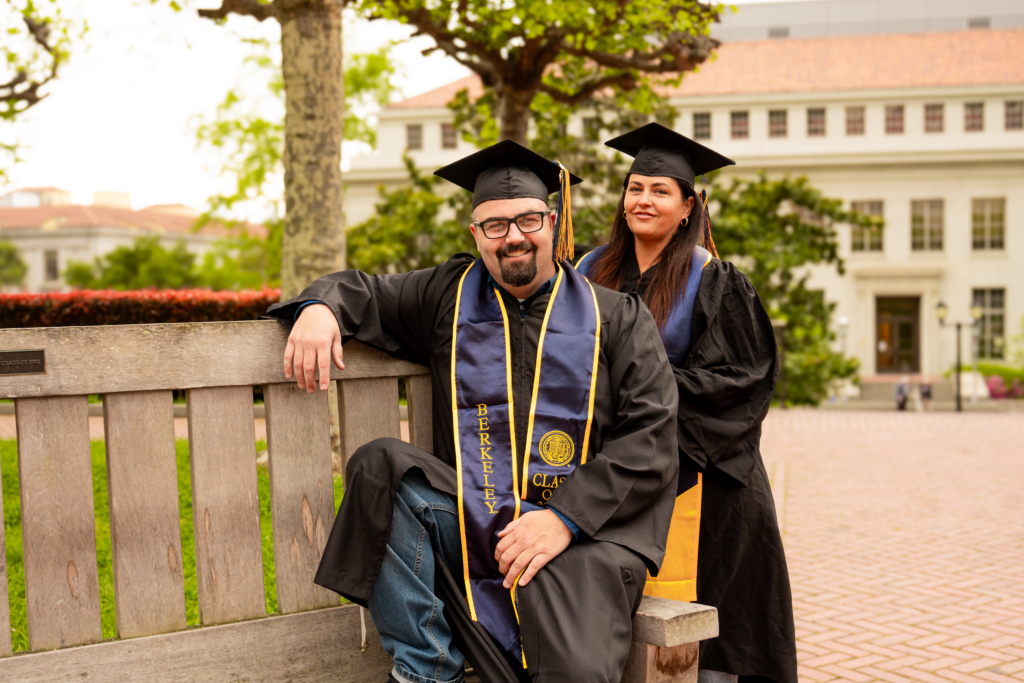 Ryan and Melissa Mattson wearing graduation gowns and regalia while posing near a bench