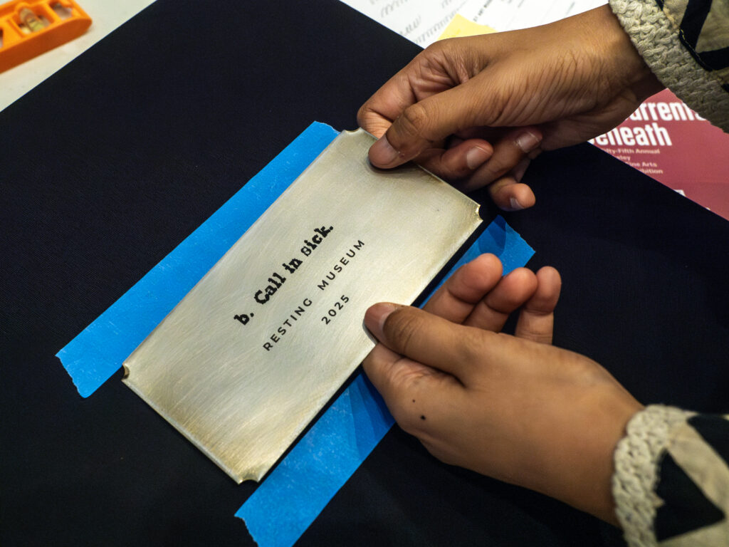 Uma foto de Priyanka d'Souza's Hands Instalando a placa de metal com o nome de sua exposição, "b. Ligue para doentes. Museu de repouso, 2025"